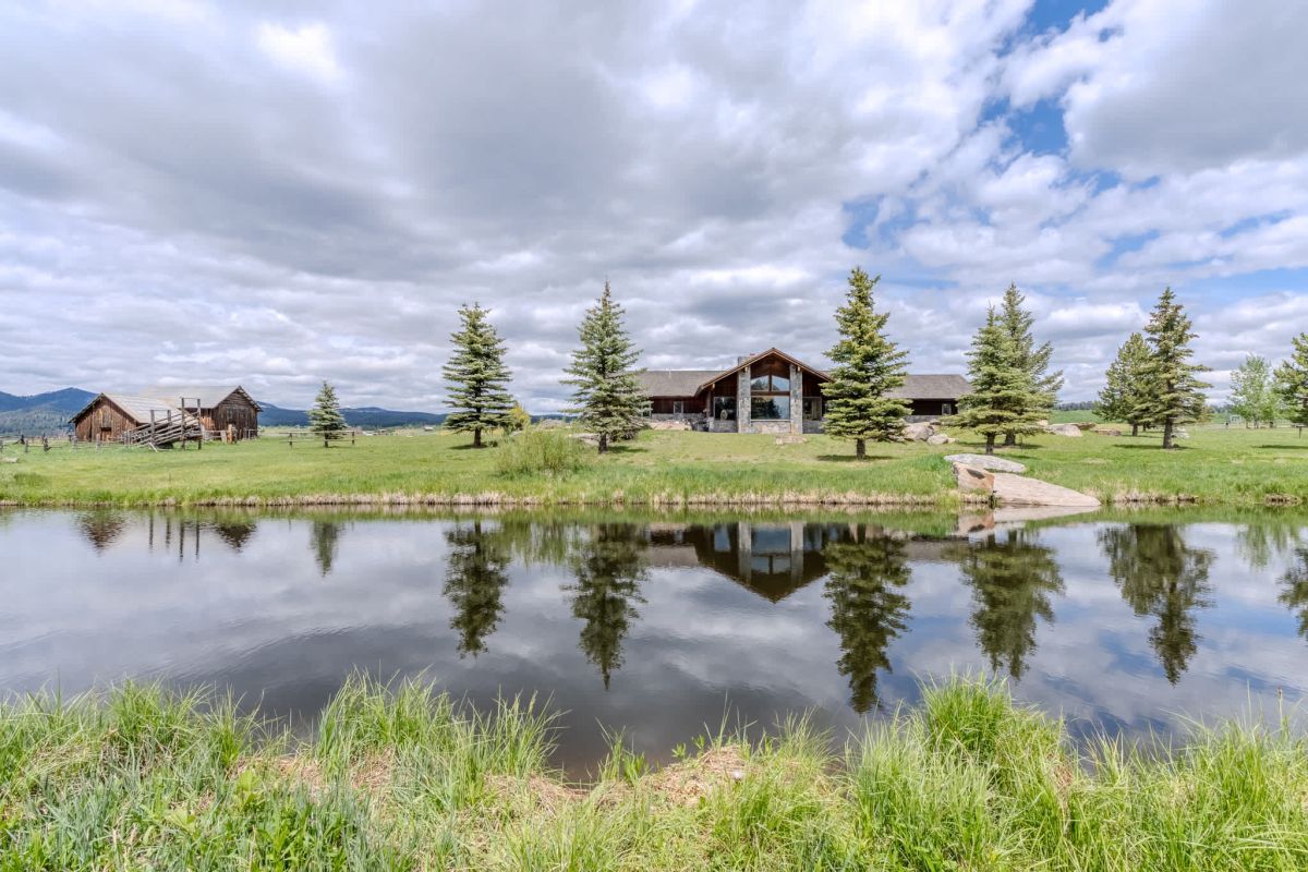 Luxury vacation rental cabin reflected in a tranquil pond surrounded by evergreen trees.